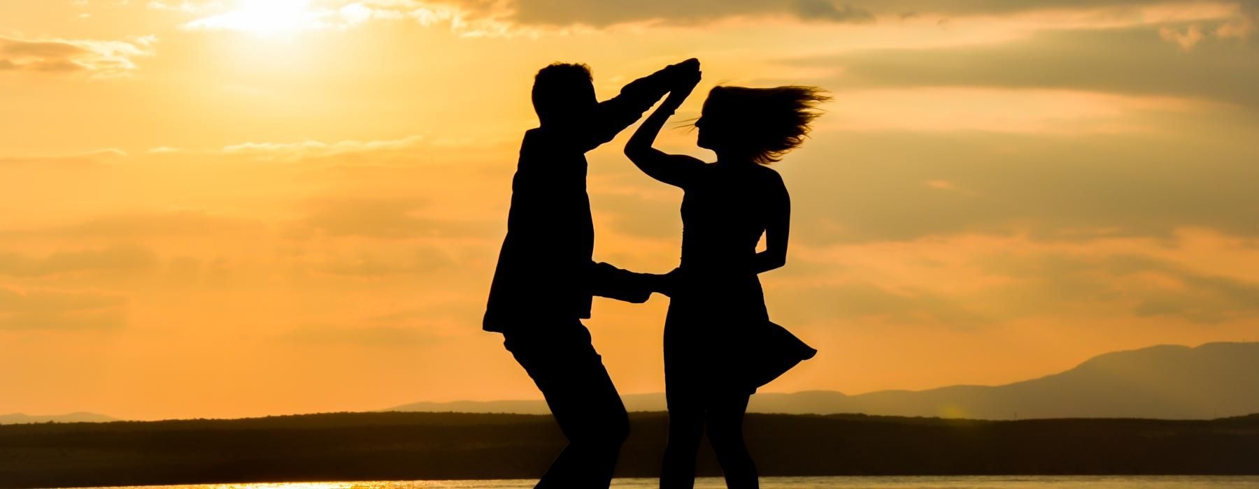 a man and woman holding dancing on a beach at sunset